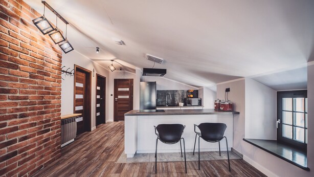 Eine moderne Küche mit Backsteinwand, Holzboden und einer zentralen Kochinsel mit zwei schwarzen Stühlen.