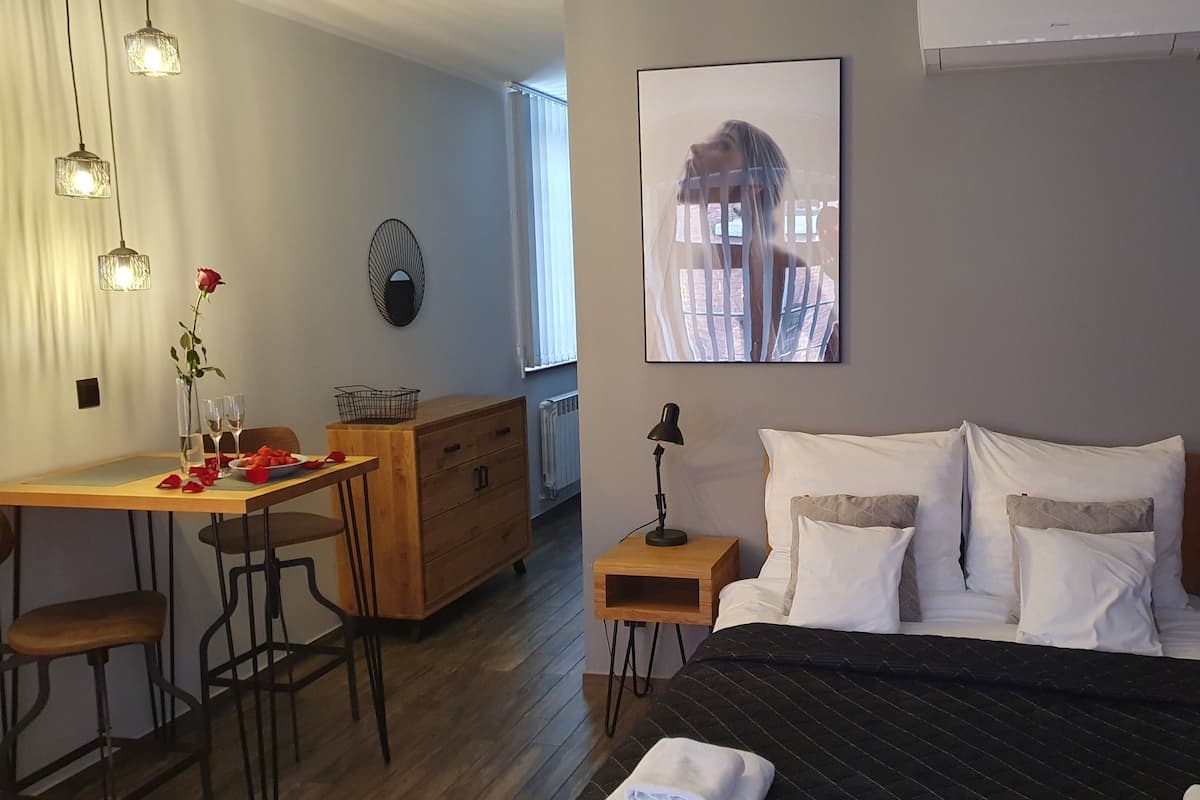 A bedroom with a bed, bedside tables, a desk, a chair, a radiator, and a window with blinds.