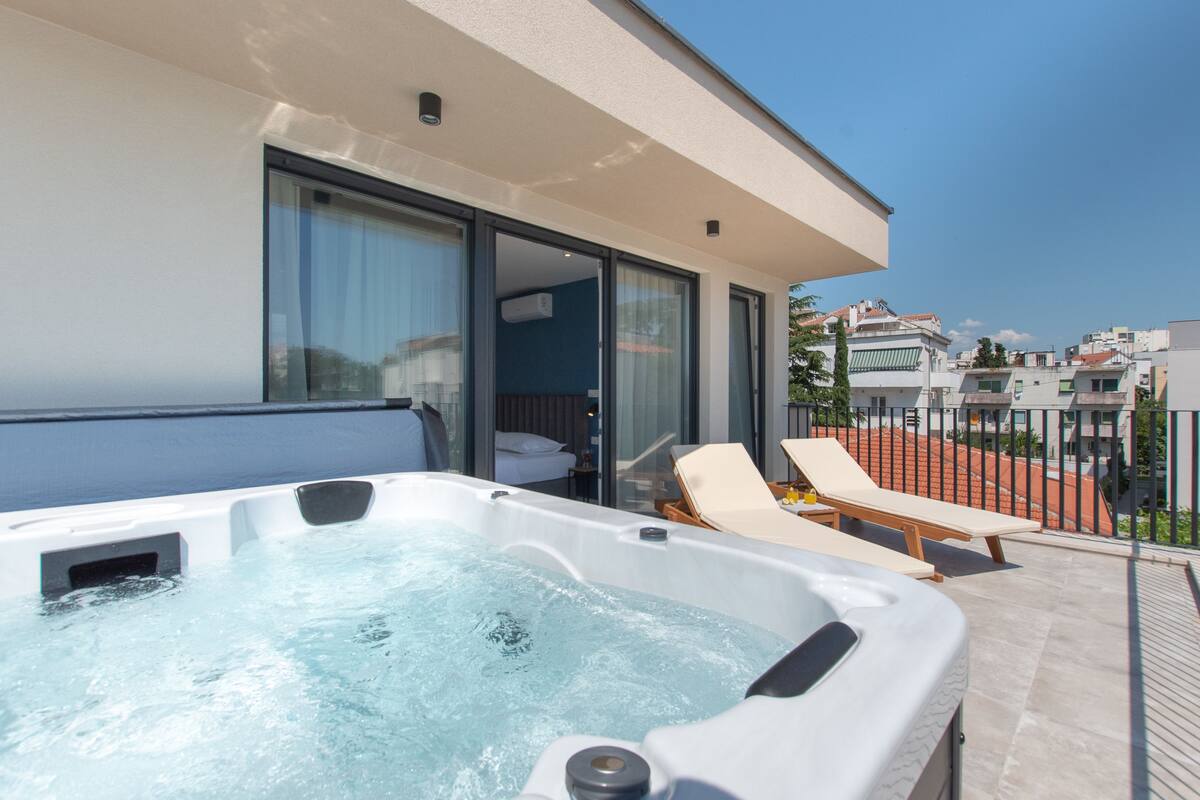 Un espacio exterior moderno con jacuzzi, sillones de descanso y una sala de cristal al fondo.