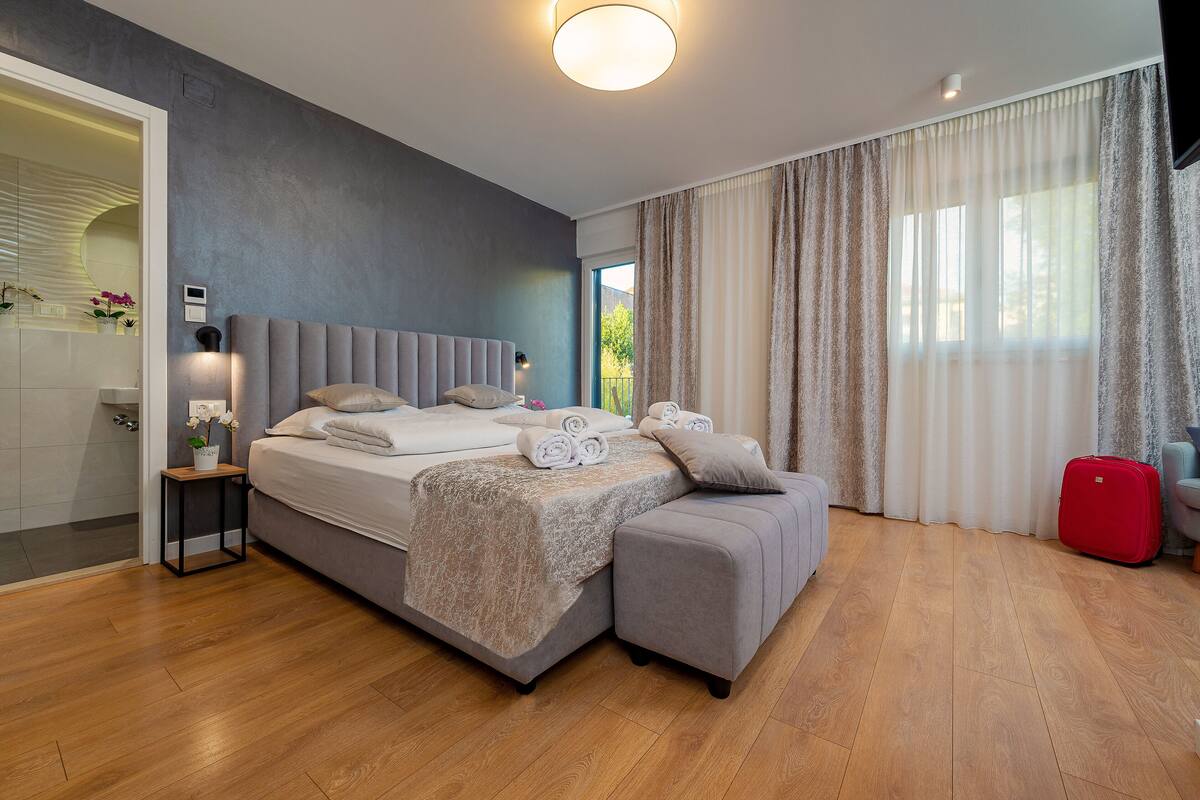 Un dormitorio moderno con una cama grande, un sofá gris y una maleta roja.