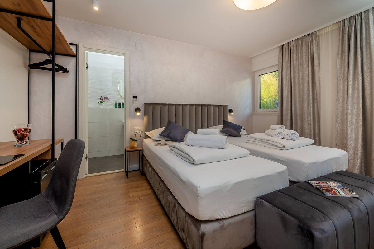 Una habitación de hotel moderna con dos camas, un escritorio, una silla y una ventana con cortinas.