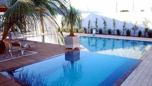 Una piscina con cubierta de madera, palmeras y un borde de azulejos.