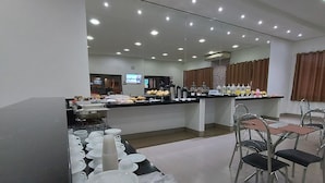 Comedor moderno de hotel con barra de buffet, que incluye platos, vasos y diversos alimentos.