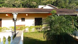 A building with a tiled roof, a balcony with white balustrades, and a lush green garden. - Pousada Atlantica Recanto do Mar (Caraguatatuba)