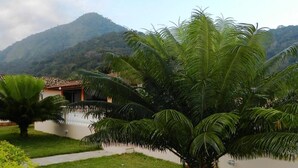 A lush garden with palm trees and a pathway leading to a building with a tiled roof. - Pousada Atlantica Recanto do Mar (Caraguatatuba)