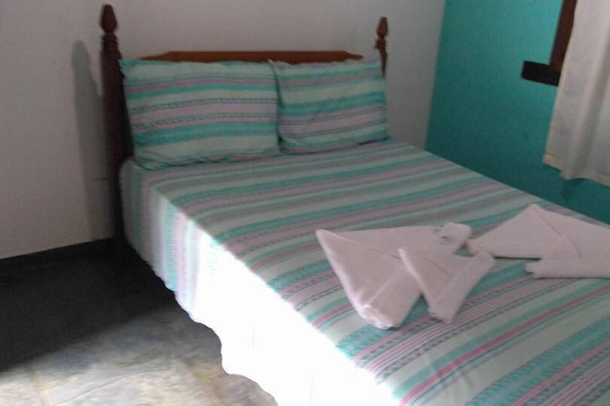 A single-bed room with a striped bedspread, pillows, and a neatly folded towel on the bed.
