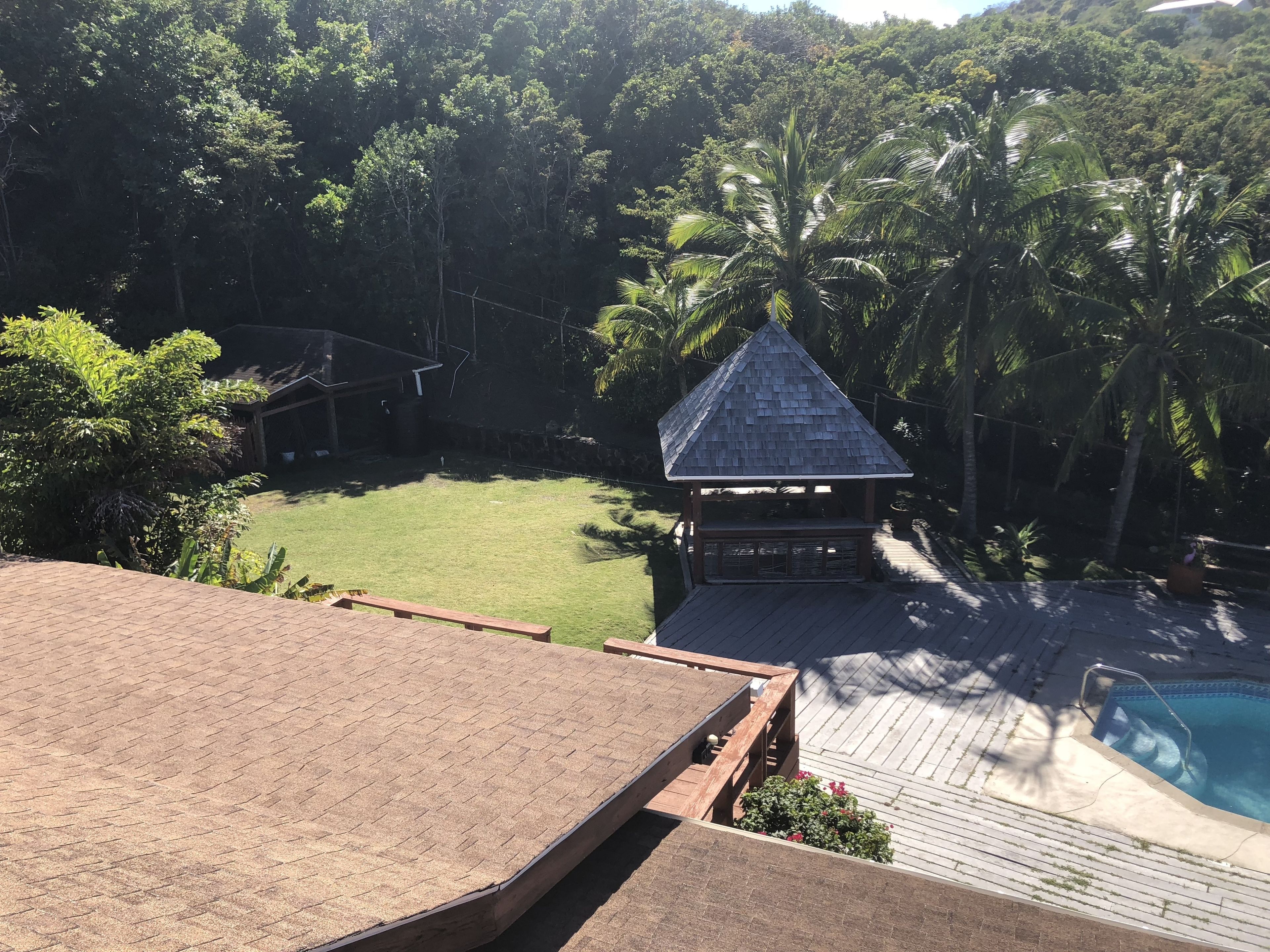 A wooden deck with a pool, a gazebo, and a grassy yard surrounded by trees.