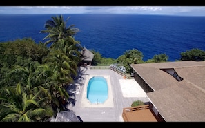 A pool with a view of the ocean, surrounded by palm trees and a wooden deck. - Chateau Devaux Cliff Top Villa (Gros Islet)