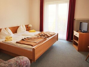 A hotel room with a bed, a television, a desk, and a window with curtains.