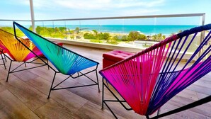 Een balkon met kleurrijke hangmatten met uitzicht op een strand en de oceaan.