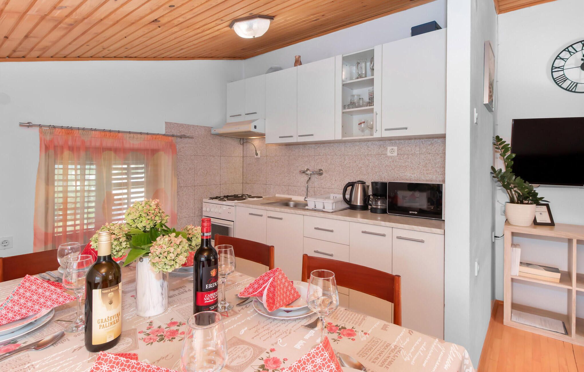 A modern kitchen with white cabinets, a microwave, and a gas stove. There is a dining table set with plates, glasses, and a bottle of wine.