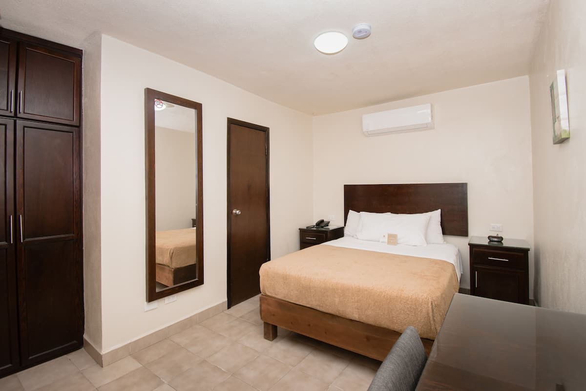Une chambre d’hôtel comprenant un lit, des tables de chevet, un bureau, une chaise, une armoire et un miroir.