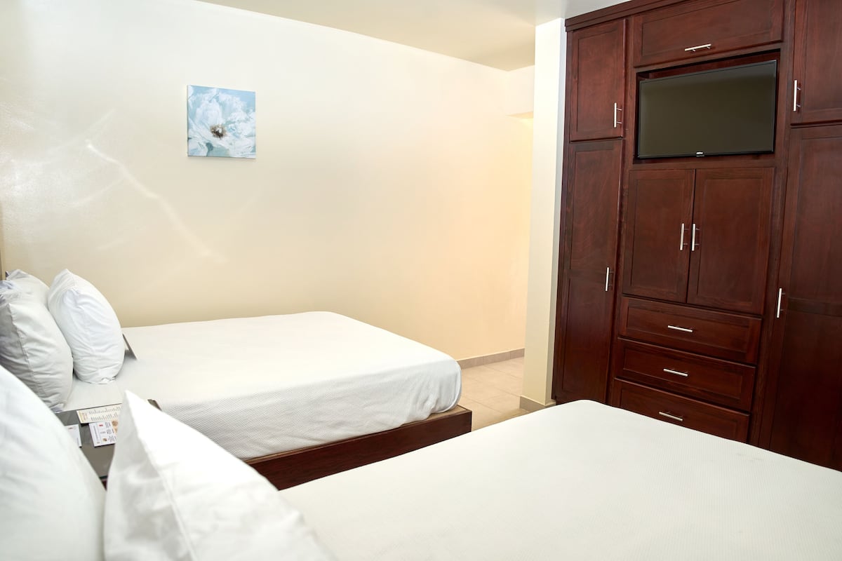 Une chambre d’hôtel avec deux lits simples, une armoire en bois équipée d’un téléviseur à écran plat, et un petit tableau accroché au mur.