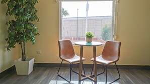 Une pièce avec une plante en pot, deux chaises, une petite table et une fenêtre donnant sur un bâtiment à l’extérieur.