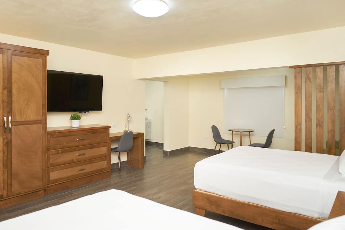 Une chambre d’hôtel dotée d’une grande armoire en bois, d’un téléviseur à écran plat fixé au-dessus d’une commode en bois, d’un petit bureau avec une chaise et d’un lit avec une literie blanche.