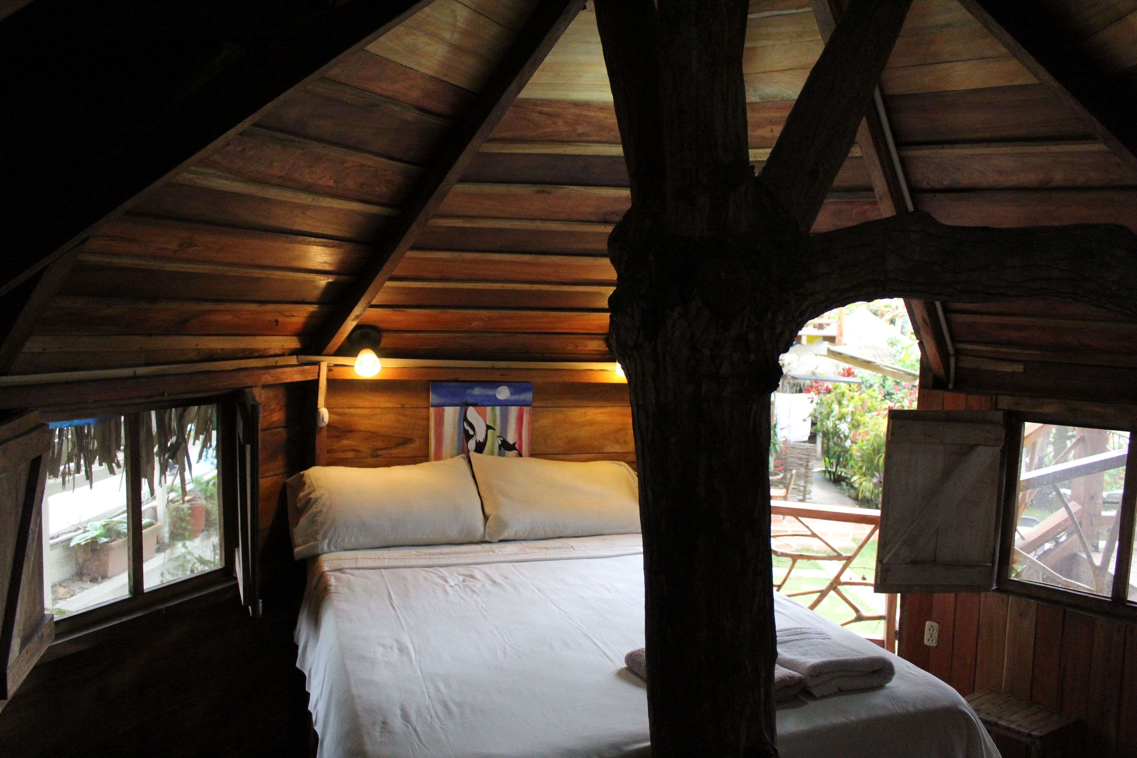 A wooden cabin bedroom with a bed, a window, and a wooden ceiling.