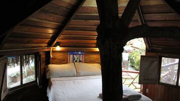 A wooden cabin bedroom with a bed, a window, and a wooden ceiling.