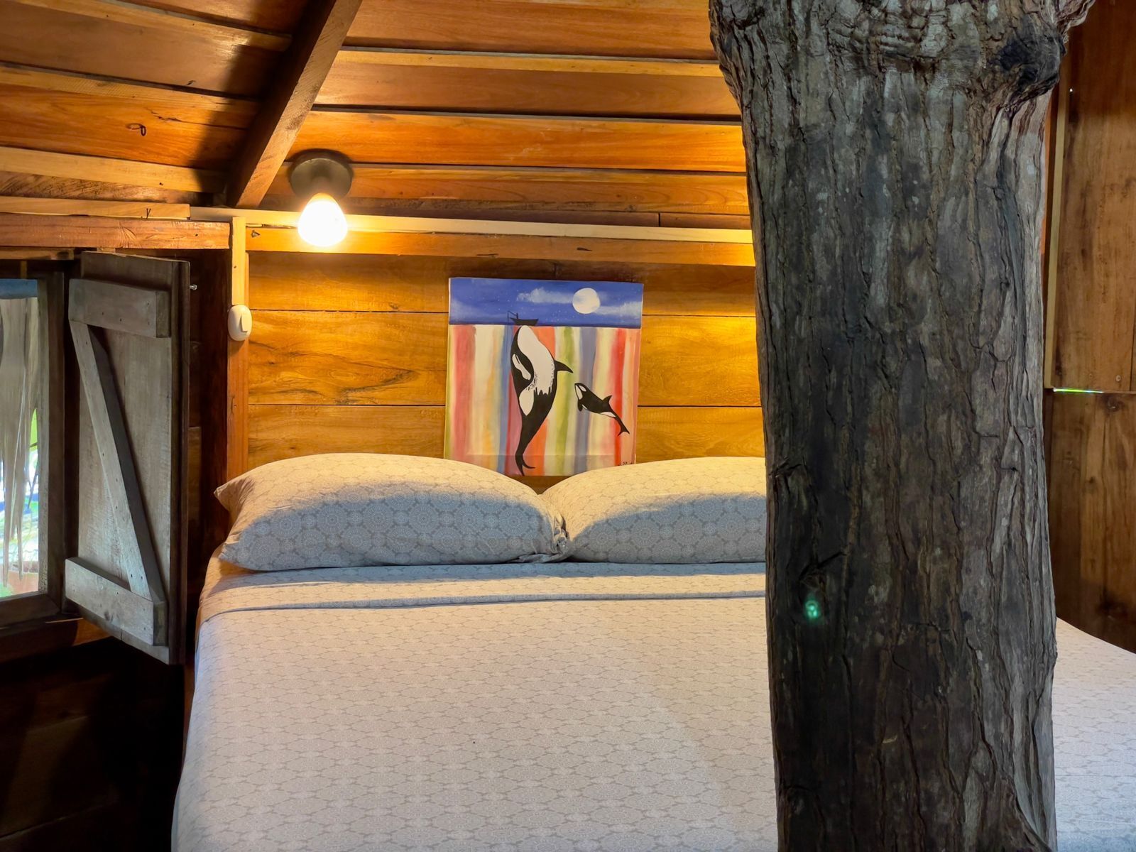 Ein Schlafzimmer einer Holzhütte mit einem Bett, einer Wandleuchte und einem Vogelbild.