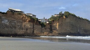 Une falaise côtière sur laquelle sont construits des bâtiments, dominant une plage de sable.