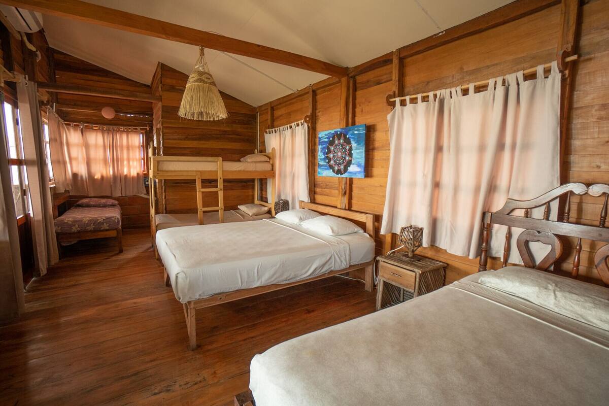 Una habitació acollidora d'estil cabana amb dos llits, una llitera, parets de fusta, una làmpada penjant i un quadre a la paret.