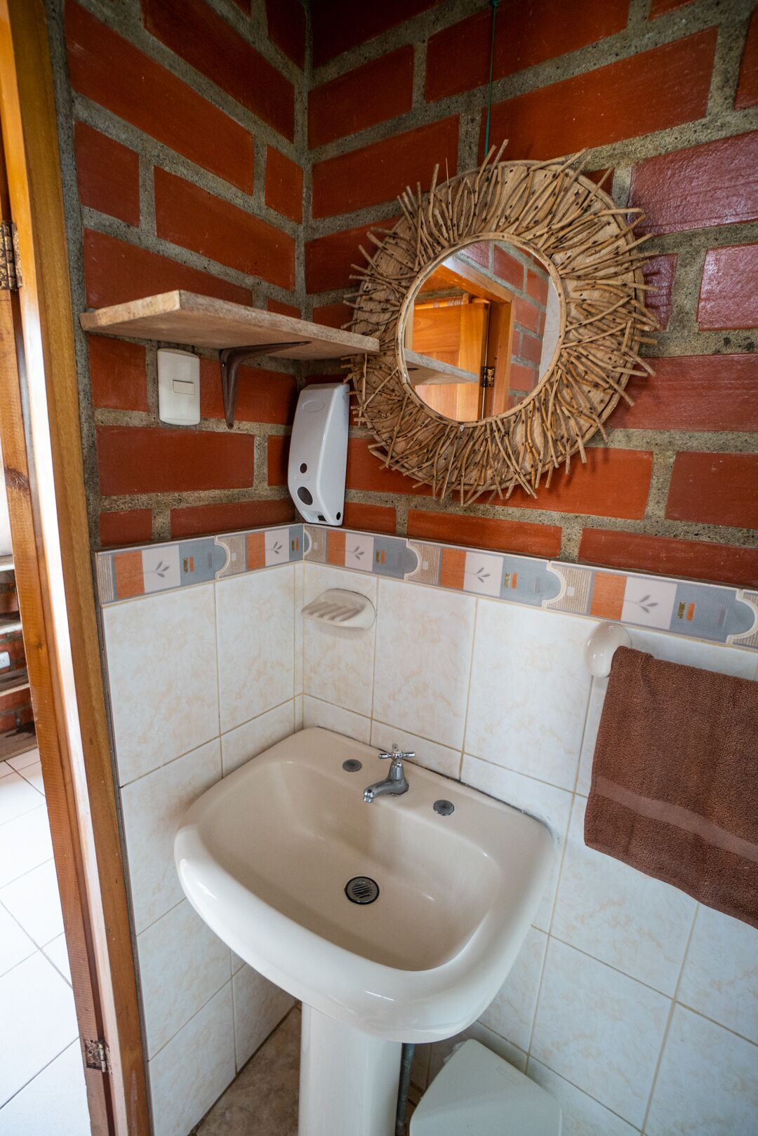 Een badkamer met een wit wastafel, een spiegel met houten lijst, een zeepdispenser en een handdoek aan de muur.