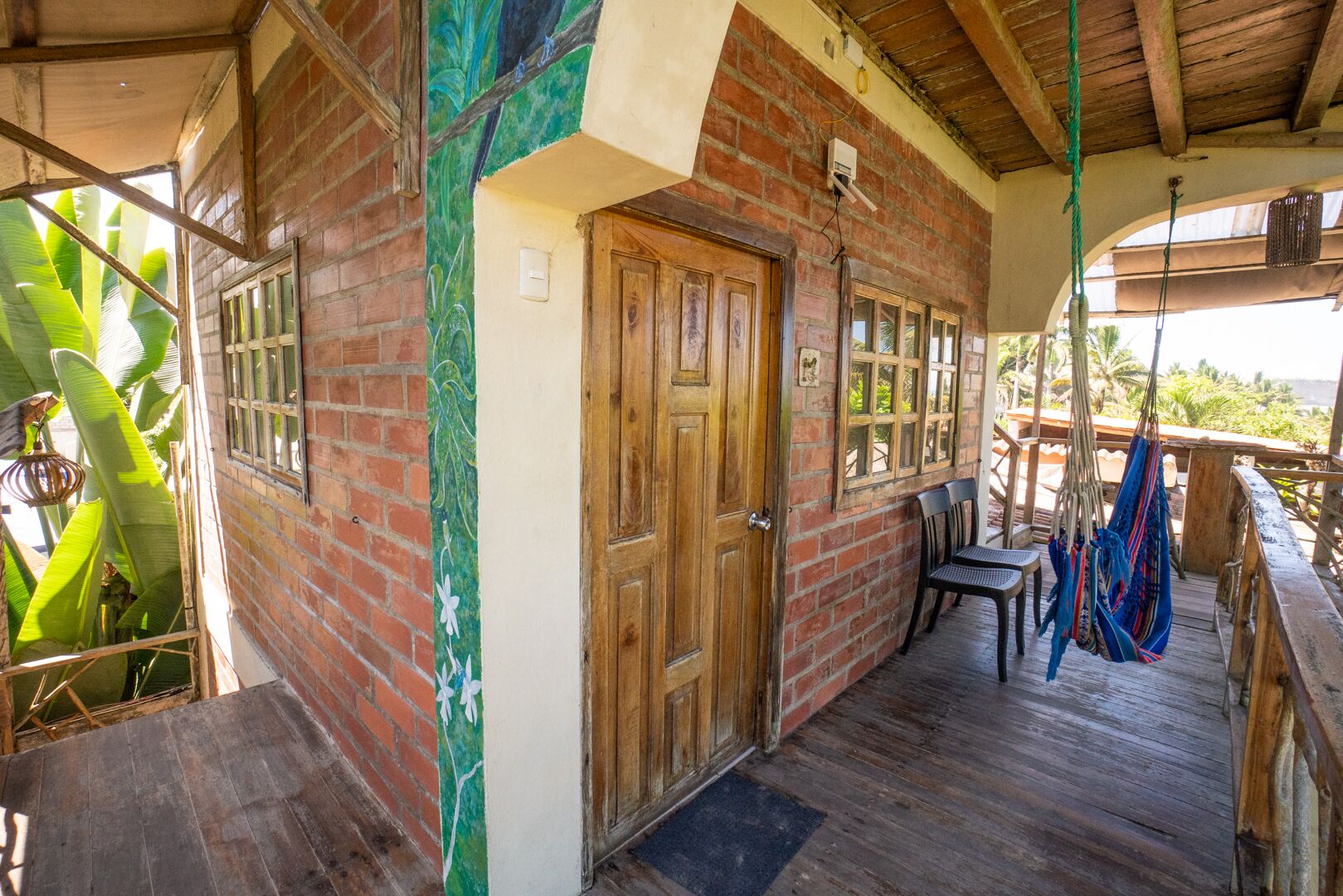 A wooden porch with a brick wall, a wooden door, and a view of the outdoors.