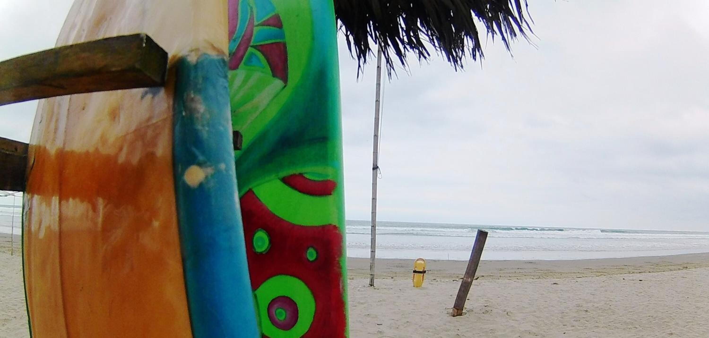 A beach scene with a surfboard leaning against a pole, a colorful umbrella, and a yellow fire hydrant on the sand.