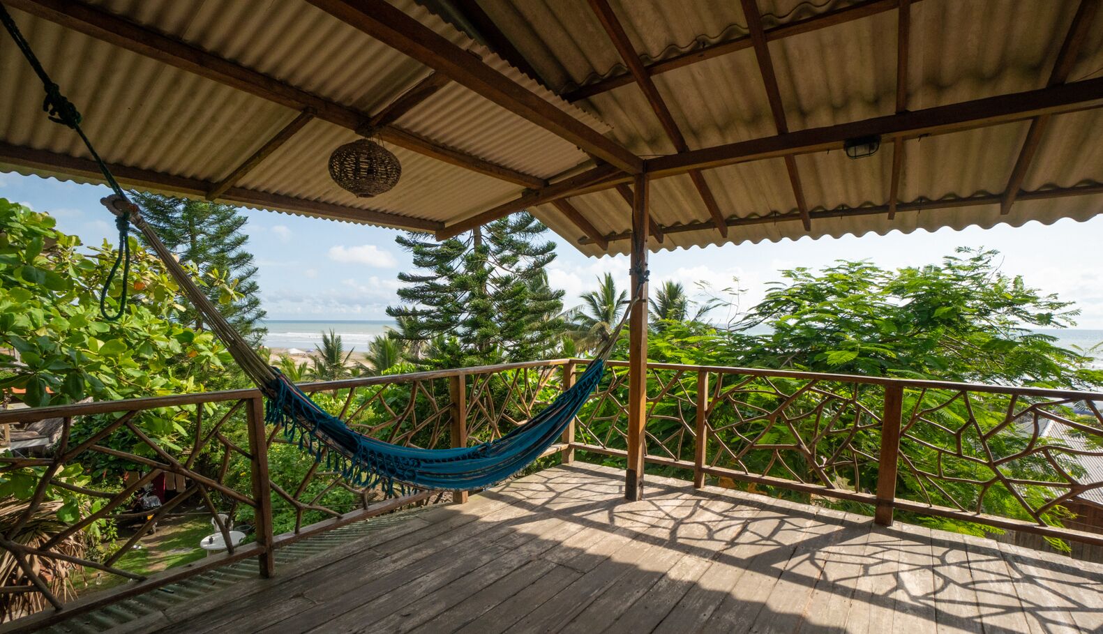 A wooden deck with a hammock, surrounded by lush greenery and a view of the ocean.