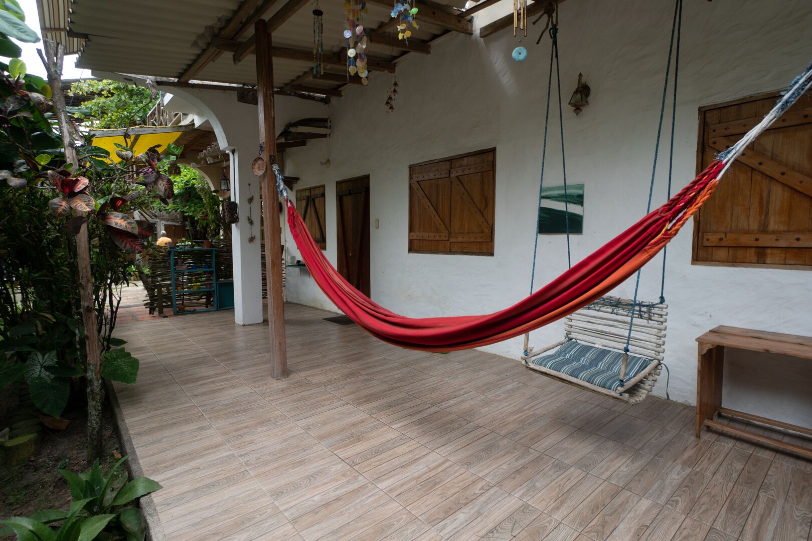 Una hamaca en un espacio exterior cubierto, con suelo de madera y paredes blancas.
