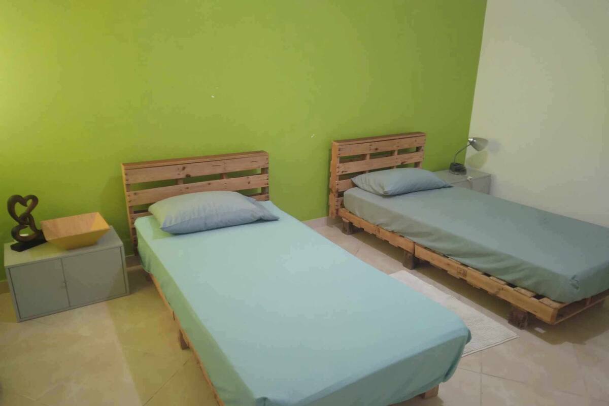 A room with two wooden beds, a small nightstand, and a green wall.