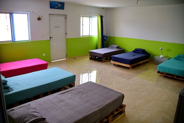 Un dormitorio con cuatro camas, una puerta, ventanas y un ventilador.
