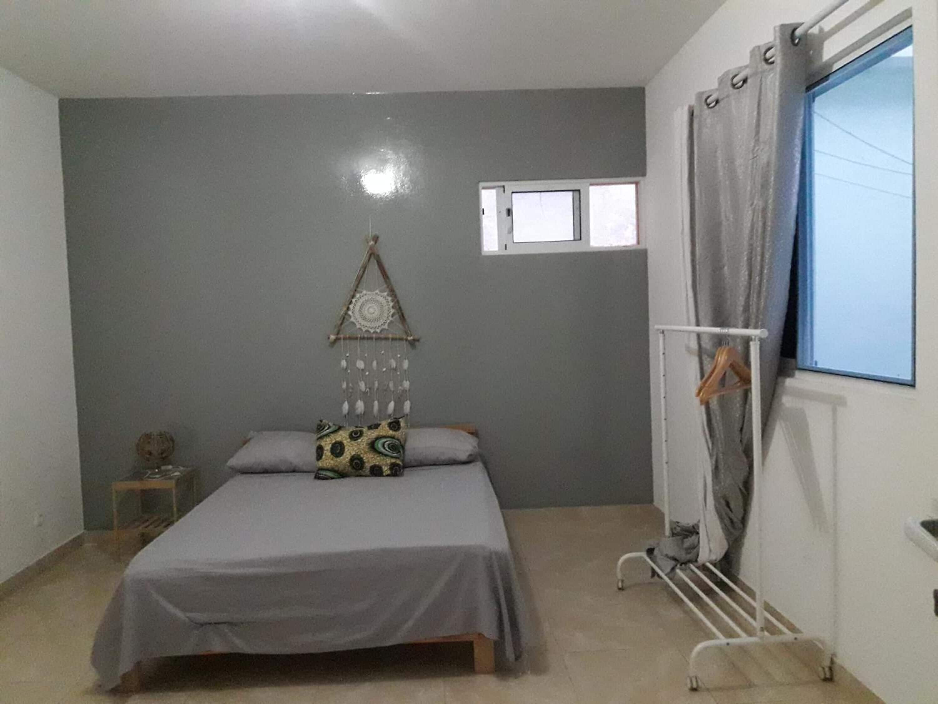 A bedroom with a bed, a small bedside table, a wall-mounted decoration, a window with curtains, and a radiator.