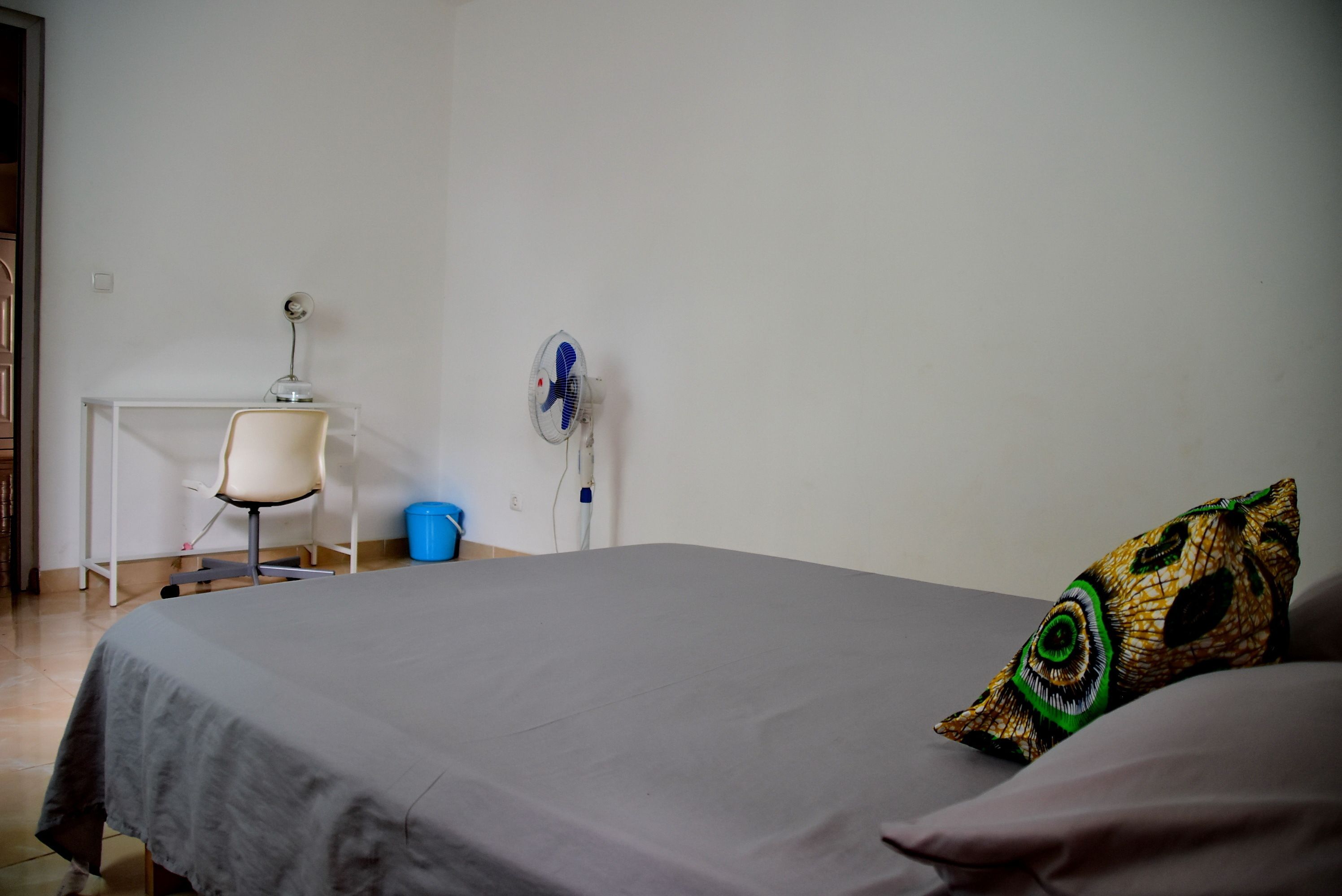 A bedroom with a bed, a desk, a chair, and a wall-mounted fan.