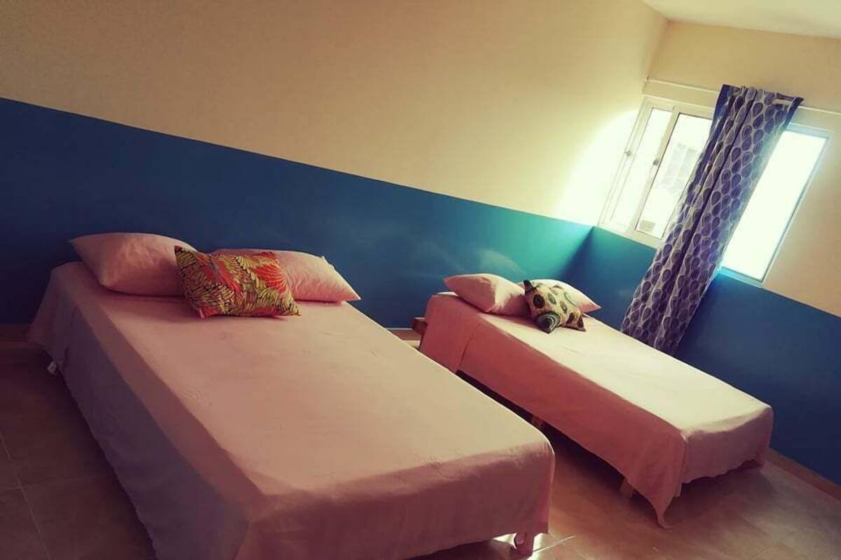 A room with two beds, each with a pink bedspread and pillows, and a window with curtains.