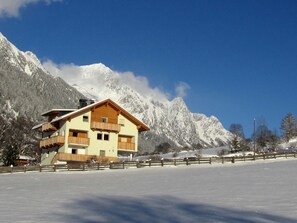 Eine zweistöckige Chalet mit Balkon, vor einer Kulisse schneebedeckter Berge und einem klaren, blauen Himmel.