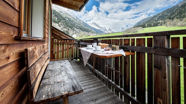 Una terraza de madera con una mesa dispuesta para el desayuno, con vistas a un paisaje montañoso.