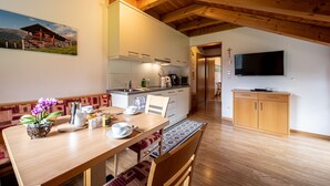 Una cocina moderna con armarios de madera, un comedor con mesa y sillas de madera, y un televisor montado en la pared.