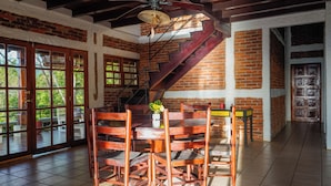 A dining area with a brick wall, wooden chairs, a table, and a ceiling fan. - Casa Ruth (San Juan del Sur)