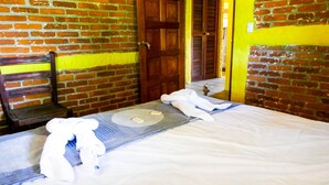 A hotel room with a brick wall, a wooden door, and a bed with white linens and towels. - Casa Ruth (San Juan del Sur)