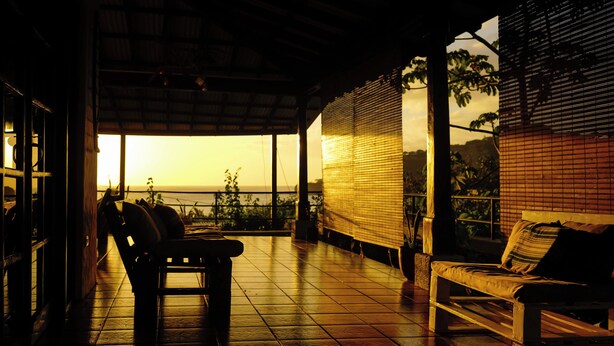 A patio with a bench and chairs, a view of the sunset, and a covered area with a tiled floor. - Casa Ruth (San Juan del Sur)