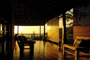 A patio with a bench and chairs, a view of the sunset, and a covered area with a tiled floor. - Casa Ruth (San Juan del Sur)