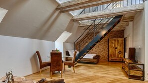 Un loft espacioso con vigas de madera a la vista, una cama de altillo, una escalera y una zona de estar acogedora con un sofá marrón.