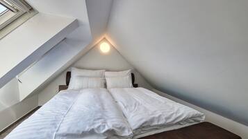 Un dormitorio con cama, almohadas y mesita de noche.