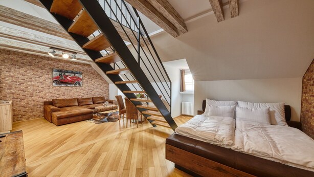 Un dormitorio estilo loft con techo inclinado, vigas de madera a la vista, una cama grande, un sofá y una mesa de comedor.