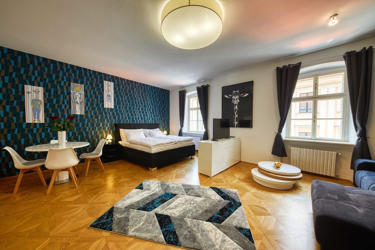 A modern bedroom with a bed, a desk, a chair, a TV, and a window with curtains.