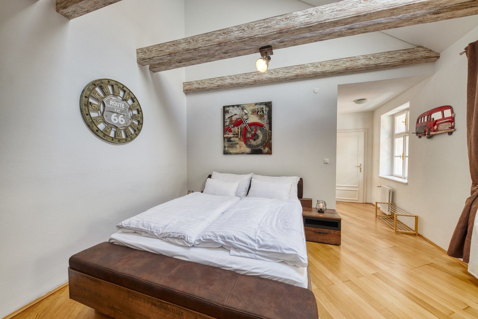 A bedroom with a wooden bed, a Route 66 clock, and a motorcycle painting.