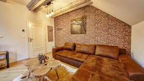 Una sala de estar con pared de ladrillo, un sofá de cuero marrón, mesas de centro de madera y techo rústico.