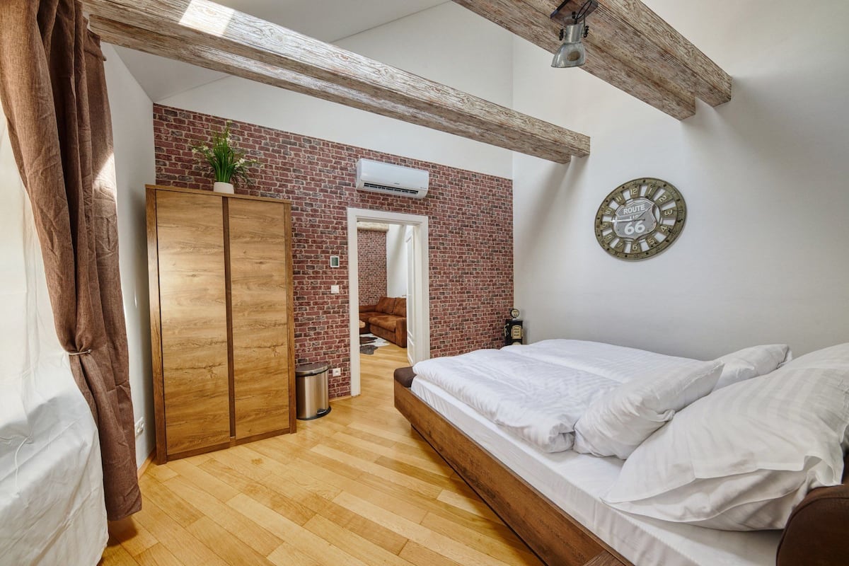 A bedroom with a wooden bed, a brick wall, a Route 66 clock, and a wooden wardrobe.