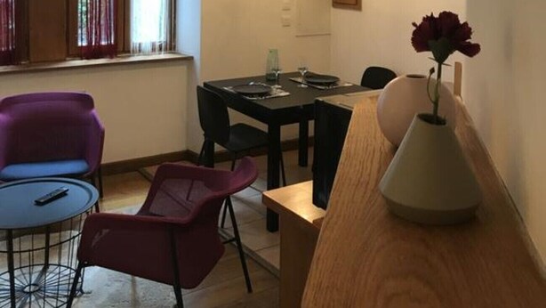 Un coin repas avec une table dressée pour quatre personnes, deux lampes suspendues, un vase avec des fleurs et une fenêtre avec des rideaux.