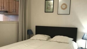 Une chambre à coucher avec un grand lit, un petit bureau avec une lampe et deux tableaux encadrés accrochés au mur.